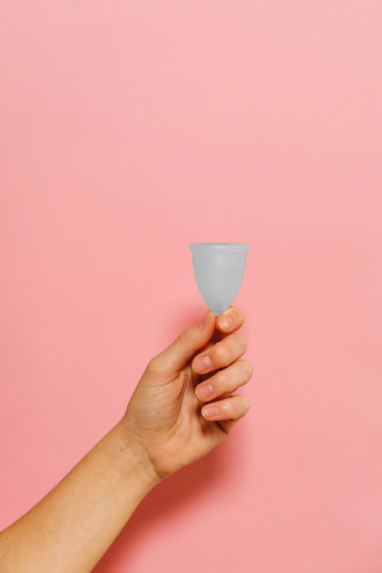 A hand holding a soft silicone menstrual cup against a blush backdrop
